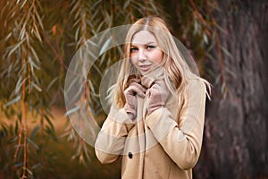 Portrait of a young beautiful woman blonde girl in a beige coat on the background of autumn Park