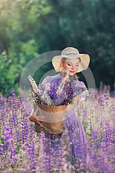 Portrait of young beautiful woman with bouquet of flowers in basket at sunny field. Pretty vintage girl in lilac dress and hat