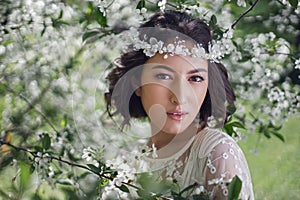 portrait of a young beautiful woman bride in white clothes standing next to a blooming cherry tree in spring. a wreath