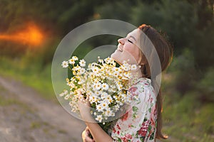 Portrait young beautiful woman with chamomile flowers at sunset.