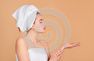 Portrait of young beautiful woman with cosmetic products. Beauty face of a cheerful attractive girl with towel on head