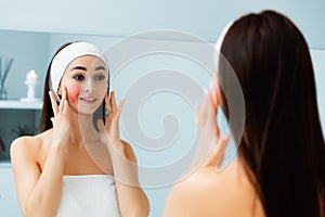 Portrait of a young beautiful woman with couperose on her cheek, looking in the mirror. Rosacea and skin care concept photo