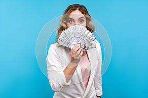 Portrait of young beautiful woman covering half face with dollar banknotes. isolated on blue background