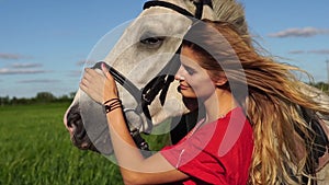 Portrait of young beautiful woman dreesed in red with white horse near the field