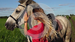 Portrait of young beautiful woman dreesed in red with white horse near the field