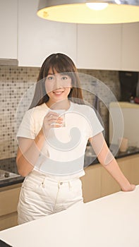 Portrait of young beautiful woman drinking glass of water in kitchen