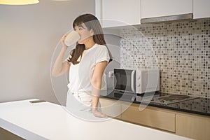 Portrait of young beautiful woman drinking glass of water in kitchen