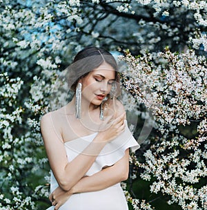 Portrait young beautiful woman fashion model posing. background blooming tree spring nature white flowers. Elegant girl