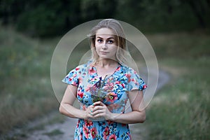 Portrait of young beautiful woman in flower dress holding flowers in her hands