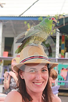 Portrait of a young beautiful woman with a green macaw standing over her hat in a nice bar in Bocas del Toro harbor photo