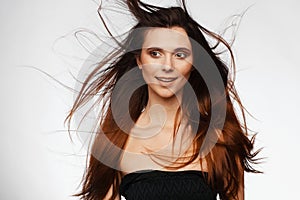 Portrait of a young beautiful woman with hair flying from the wind and bare shoulders. Studio photo