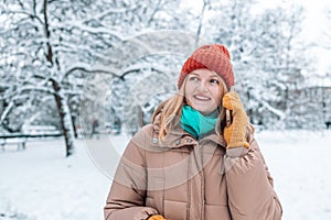 Happy young lady having mobile phone conversation on Xmas eve outdoors in winter time. Millennial woman calling on