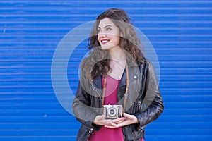 portrait of a young beautiful woman holding a vintage camera over blue background. Lifestyles. Casual clothing. Happy.