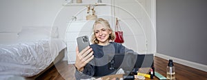 Portrait of young beautiful woman, lifestyle vlogger, sitting on bedroom floor, recording video on digital camera, using