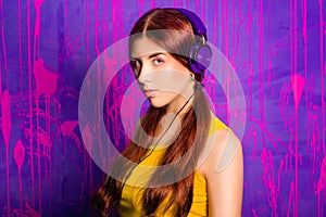 Portrait of a young, beautiful woman with long hair listening to music on headphones. Studio photo on abstract, purple background.