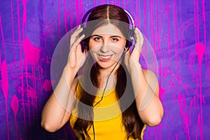 Portrait of a young, beautiful woman with long hair listening to music on headphones. Studio photo on abstract, purple background.