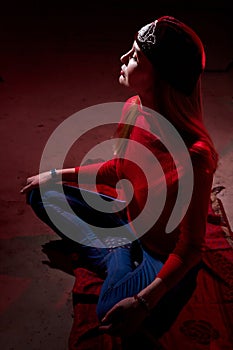 Portrait of a young beautiful woman in with long hair in a Tatar red hat and a red sweater. Fashion photo shoot in low key