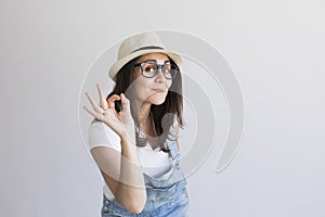 portrait of a young beautiful woman with modern glasses and hat. White background. Millennial. Hipster and lifestyle.Making the ok