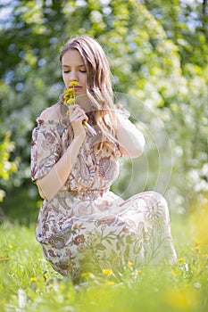 Portrait of a young beautiful woman in an original light dress inhaling the fragrance of fresh flowers sitting on the lawn of a Pa