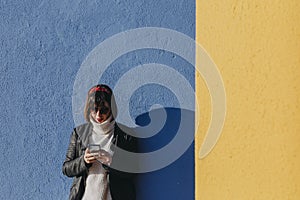 portrait of a young beautiful woman outdoors using mobile phone over blue and yellow background. Lifestyle and fun concept