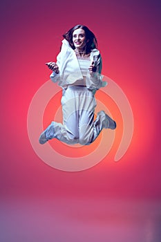 Portrait of young beautiful woman posing in a jump isolated over red background in neon light. Feeling good