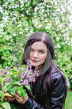Portrait of young beautiful woman with purple lilac flowers in rainy weather on background of spring blooming garden