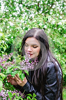 Portrait of young beautiful woman with purple lilac flowers in rainy weather on background of spring blooming garden