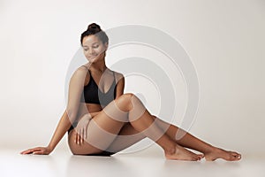 Portrait of young beautiful woman sitting on floor, posing in black underwear  over gray backgoround. Anti