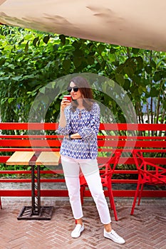 Portrait of a young beautiful woman sitting in an outdoor cafe on an open beautiful terrace drinking coffee