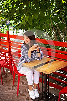 Portrait of a young beautiful woman sitting in an outdoor cafe on an open beautiful terrace drinking coffee