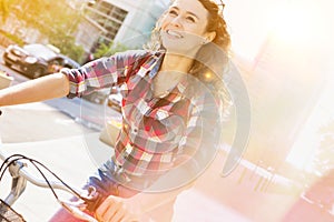 Portrait of young beautiful woman smiling while riding bicycle in the middle of the city with lens flare in background