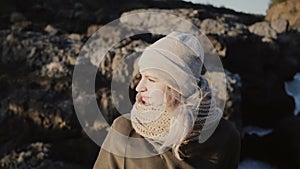 Portrait of young beautiful woman standing near the mountain and looking around, hair waving on wind in sunny day.