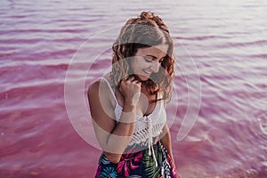 Portrait of young beautiful woman standing by a pink lake or lagoon in a natural park at sunset. Torrevieja, Spain.Tourism and