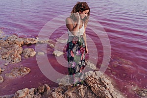 Portrait of young beautiful woman standing by a pink lake or lagoon in a natural park at sunset. Torrevieja, Spain.Tourism and