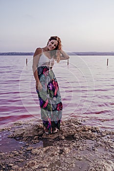 Portrait of young beautiful woman standing by a pink lake or lagoon in a natural park at sunset. Torrevieja, Spain.Tourism and