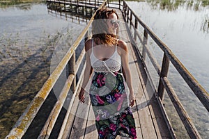 Portrait of young beautiful woman standing on a wood pier in a natural park at sunset. Tourism, love and travel concept