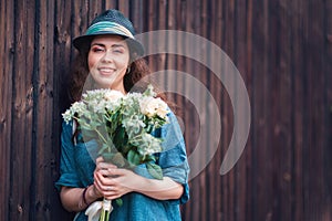 Portrait of a young beautiful woman in a straw hat holding a bouquet of white roses, against the background of a wooden