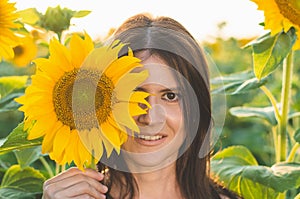 Portrait of a young beautiful woman in sunflowers. Woman covers half of her face with a sunflower