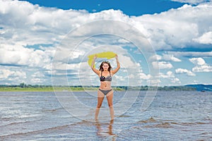 Portrait of a young beautiful woman in a swimsuit in a yellow raincoat and yellow rubber boots on a sandy beach