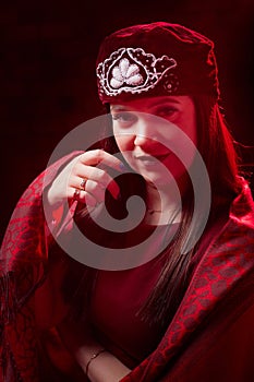 Portrait of a young beautiful woman in Tatar national folk red hat and a red dress. Fashion photo shoot in low key