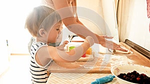 Portrait of young beautiful woman teaching her little child boy making cookies and baking pies on kitchen at home