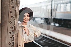 Portrait of young beautiful woman traveler in casual coat and hat who is waiting for a train on the platform of the railway statio