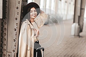 Portrait of young beautiful woman traveler in casual coat and hat who is waiting for a train on the platform of the railway statio