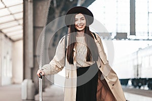 Portrait of young beautiful woman traveler in casual coat and hat who is waiting for a train on the platform of the railway statio