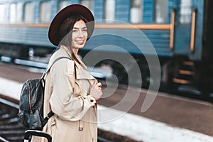 Portrait of young beautiful woman traveler who is waiting for a train on the platform of the railway station