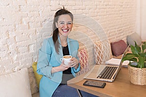 Portrait of a young beautiful woman using mobile phone in a restaurant. She is smiling. Modern life of a blogger with computer