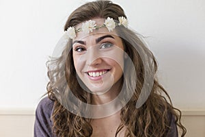 Portrait of a young beautiful woman wearing a flowers wreath. She is smiling, indoors. Lifestyle