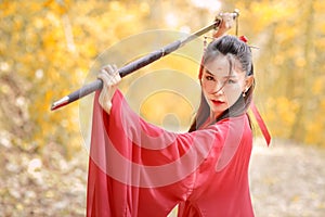 Portrait of young and beautiful woman wearing red chinese warrior costume with black sword, she post using sword among yellow