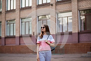 Portrait of young beautiful woman wearing sunglasses walking by city street. Lifestyle concept