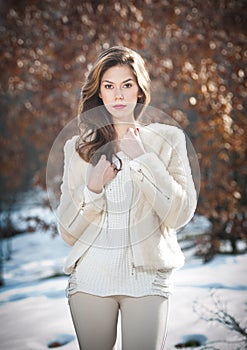 Portrait of young beautiful woman wearing white clothes outdoor. Beautiful brunette girl with long hair posing outdoor in winter